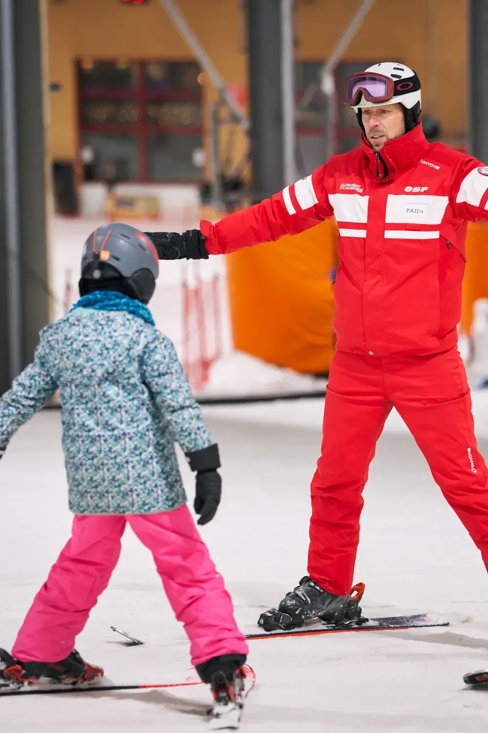 Moniteur ESF guidant une jeune élève en cours particulier sur la piste indoor